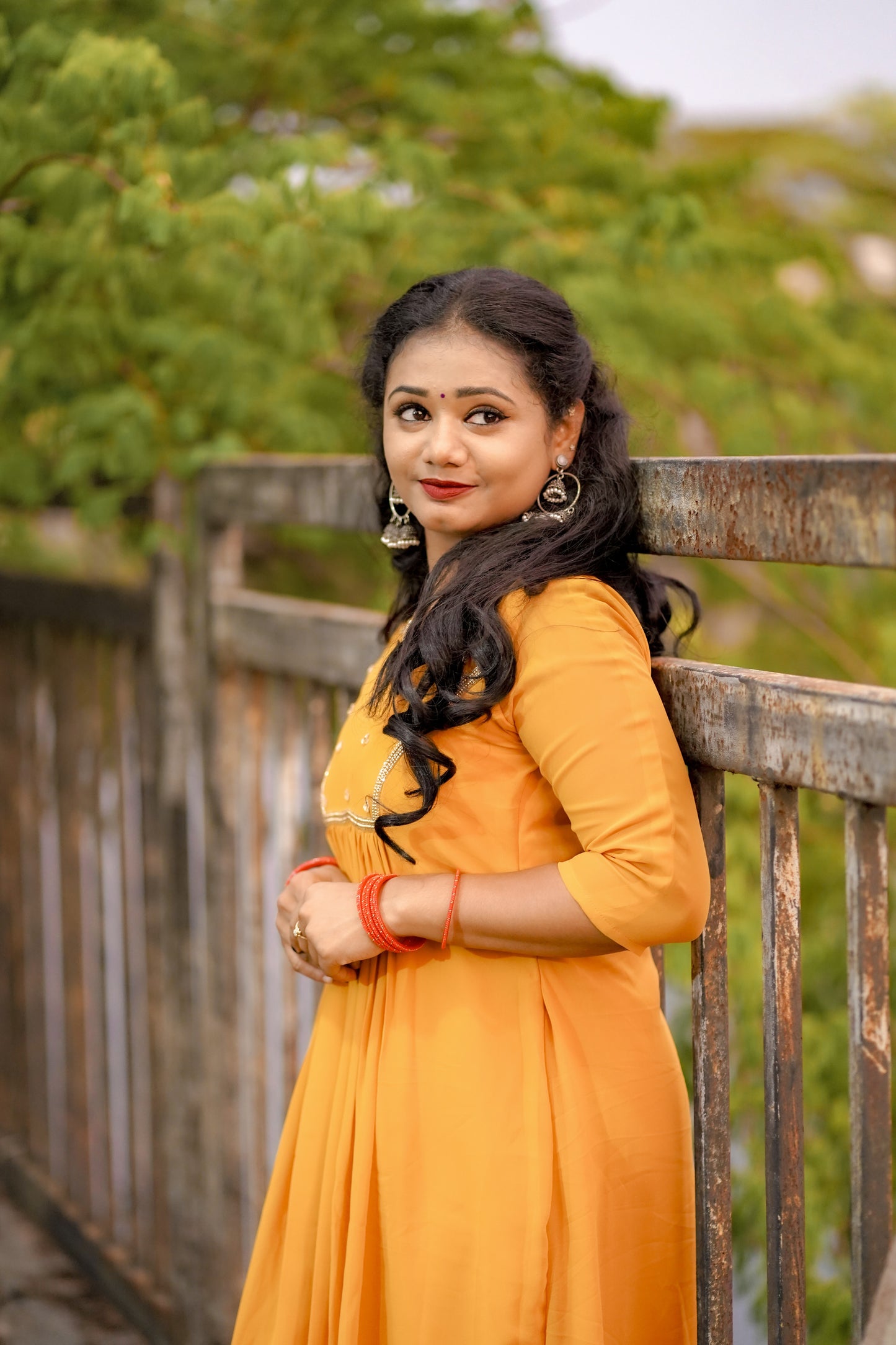 Woman wearing a mustard yellow below‑knee midi dress with hand‑beaded yoke in natural outdoor setting