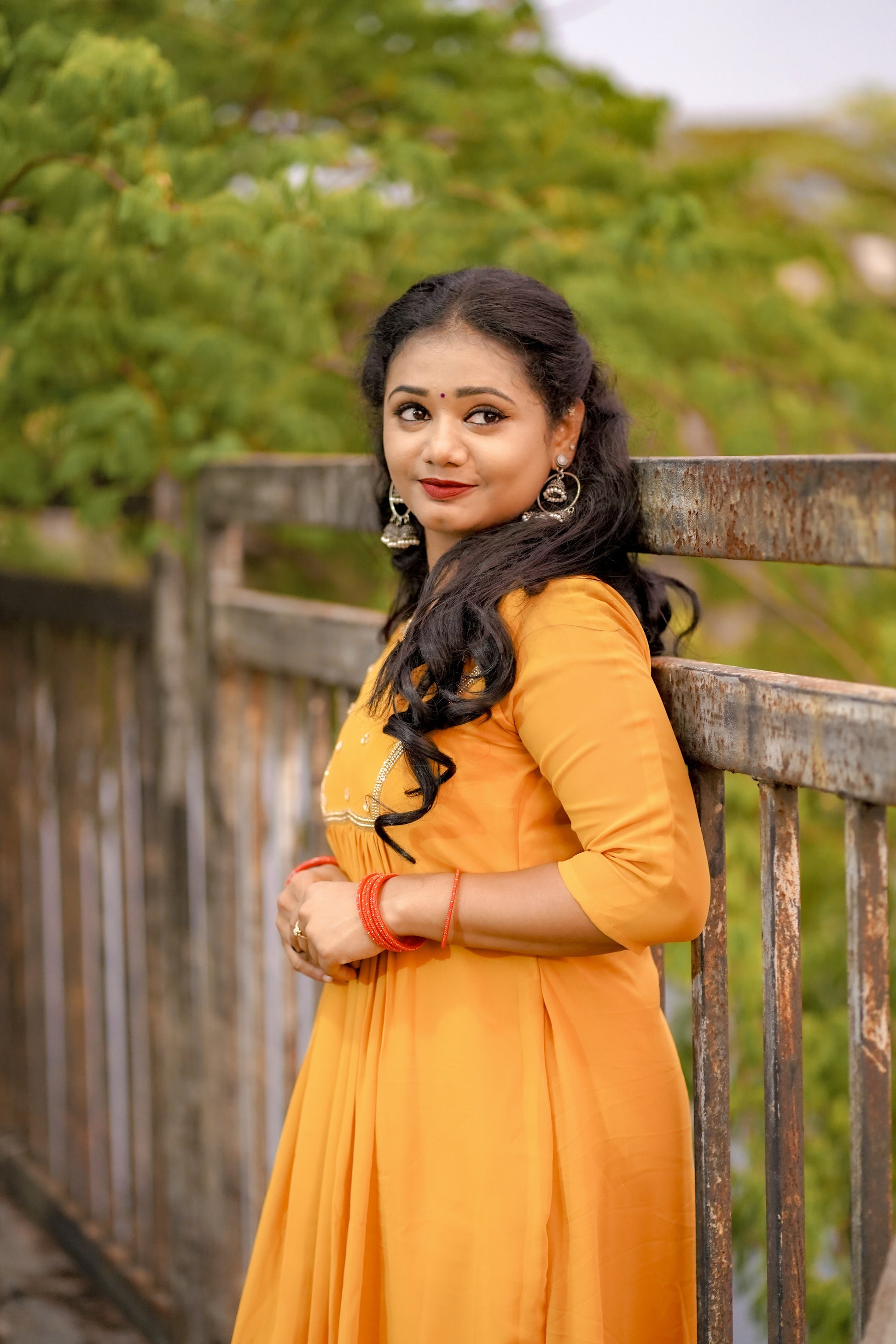 Woman wearing a mustard yellow below‑knee midi dress with hand‑beaded yoke in natural outdoor setting