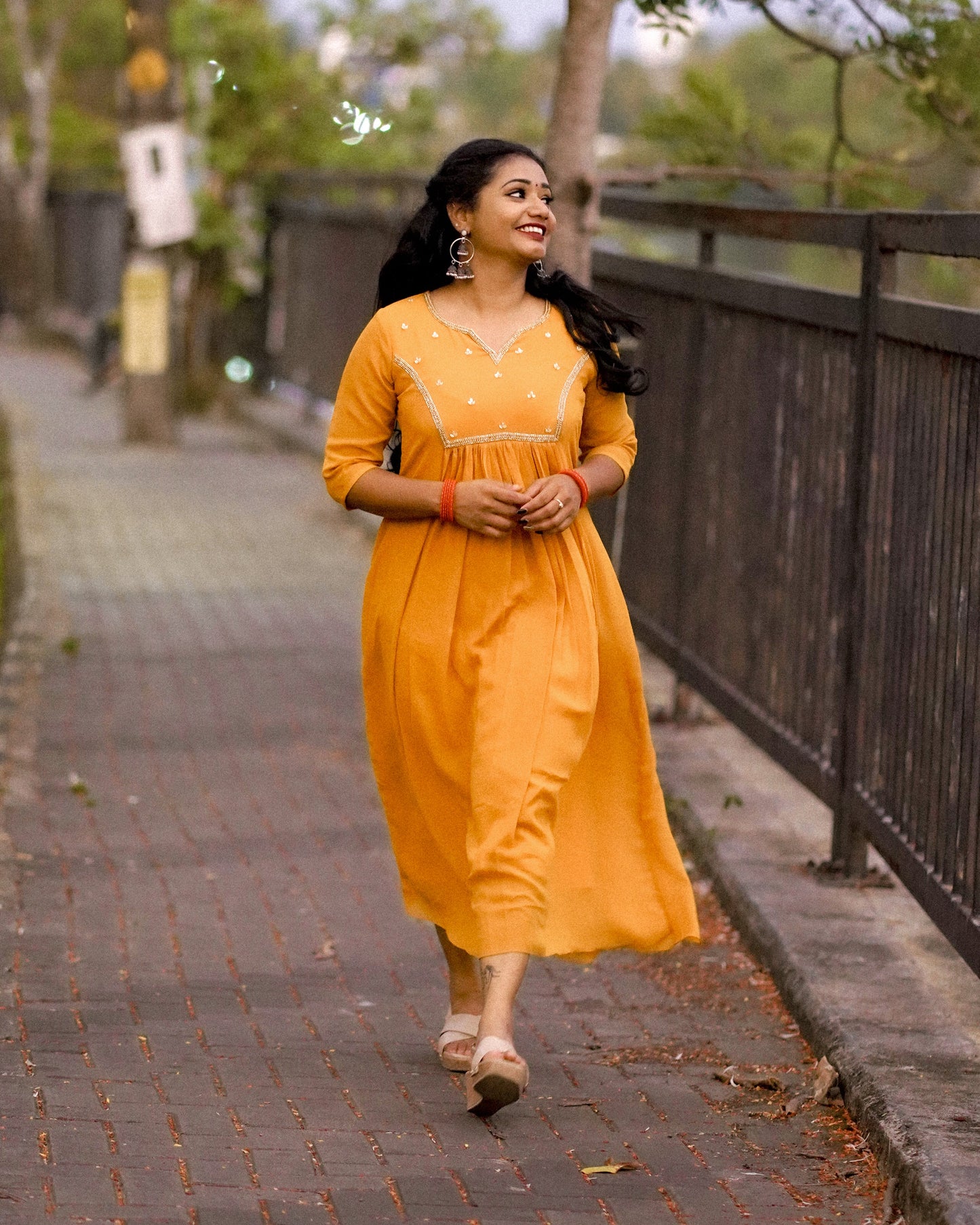 Woman wearing a mustard yellow below‑knee midi dress with hand‑beaded yoke in natural outdoor setting