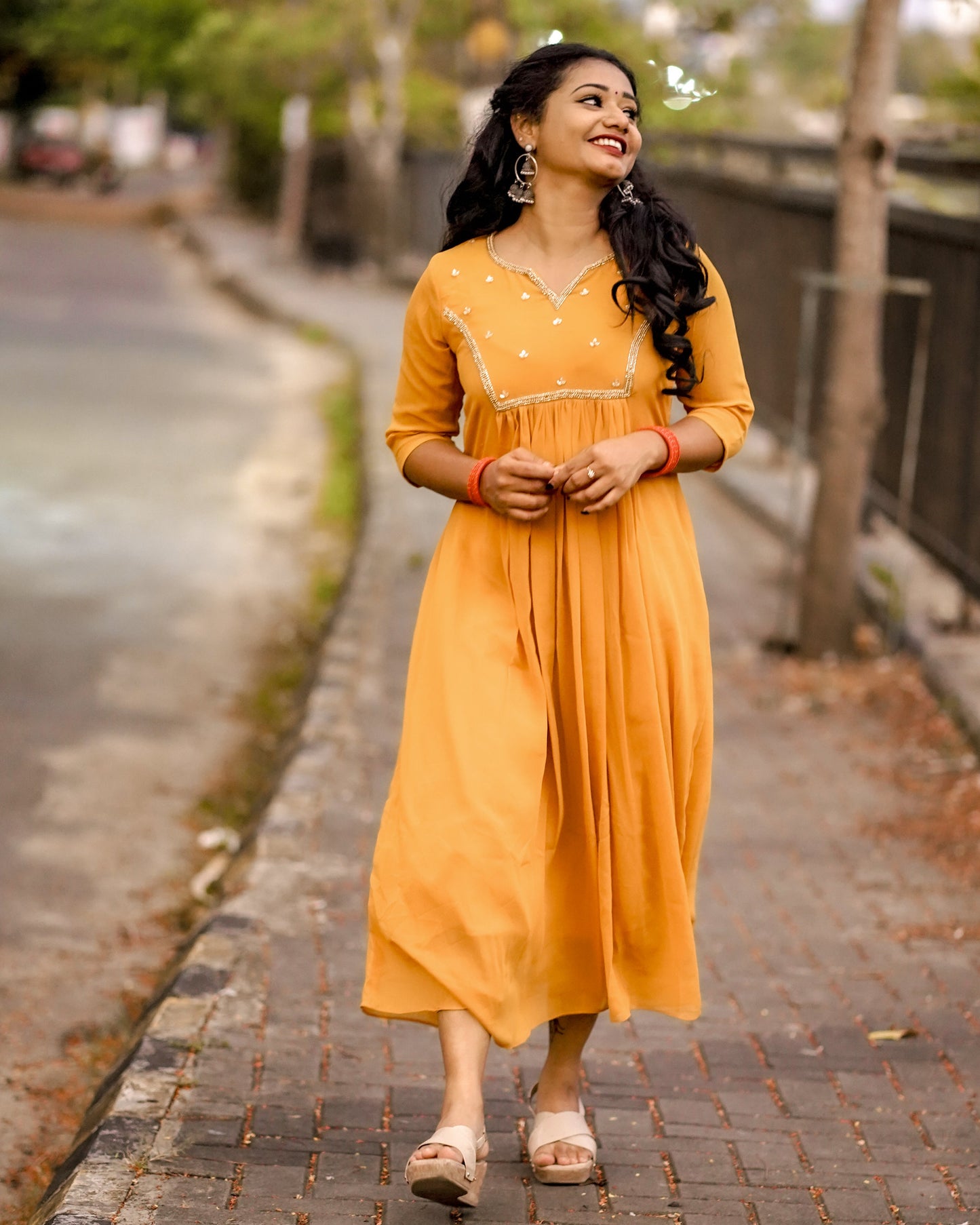 Woman wearing a mustard yellow below‑knee midi dress with hand‑beaded yoke in natural outdoor setting