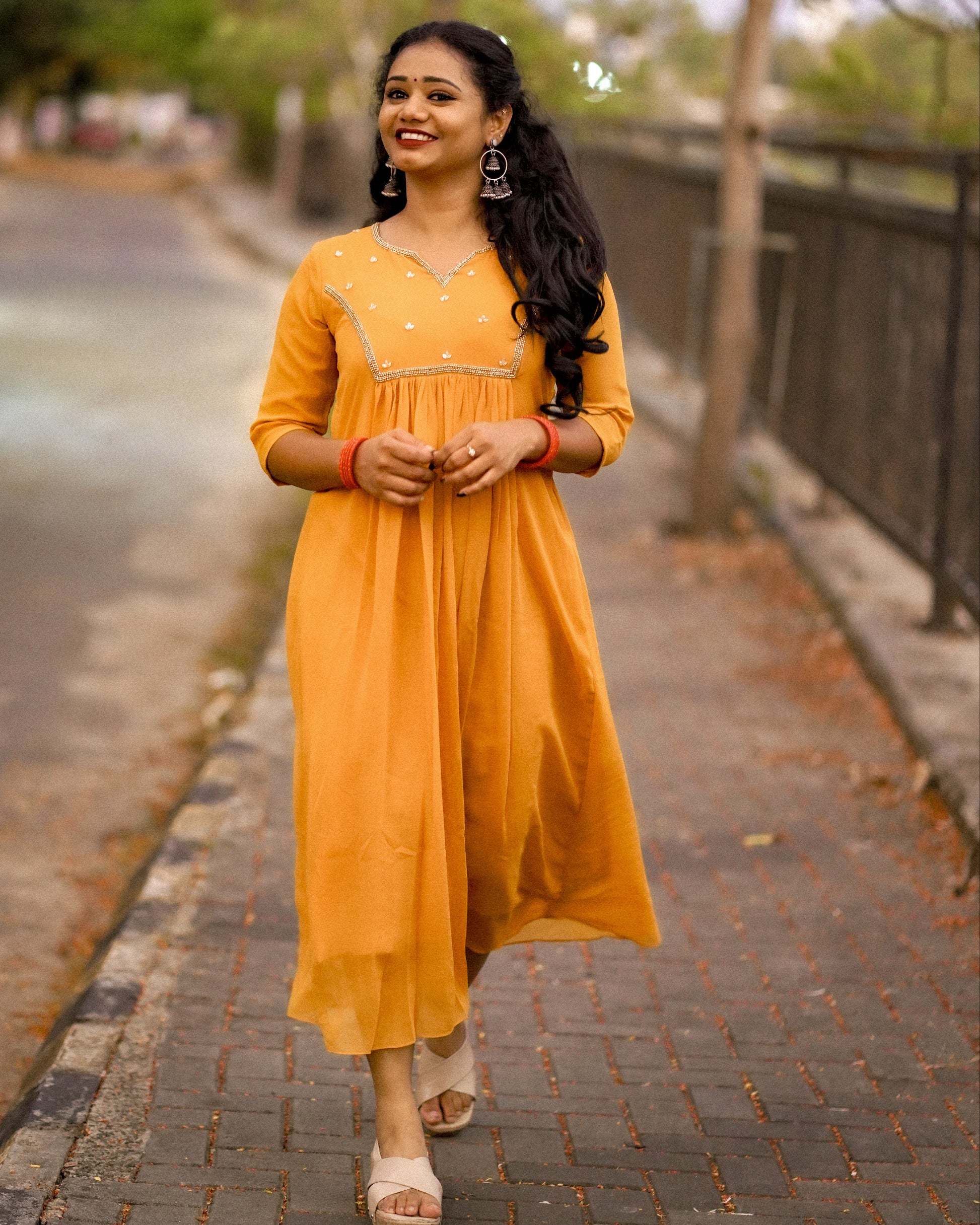 Woman wearing a mustard yellow below‑knee midi dress with hand‑beaded yoke in natural outdoor setting